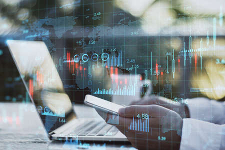 Close up of hands using laptop and smartphone at desktop with coffee cup, map and creative growing financial forex chart graph on blurry outdoor workplace background. Market, stock and trading concept. double exposureの写真素材