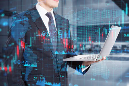 Young man with laptop with map and creative growing financial forex chart graph on blurry office...