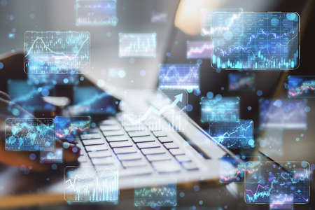 Close up of backlit female hands using laptop on desktop with creative business forex chart hologram...