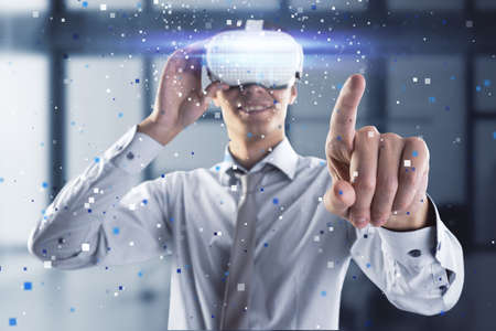 Attractive young european man pointing at abstract hologram with VR glasses in blurry office...