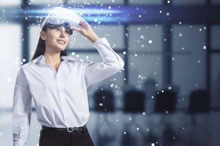 Attractive young european businesswoman with abstract hologram and VR glasses in blurry office...