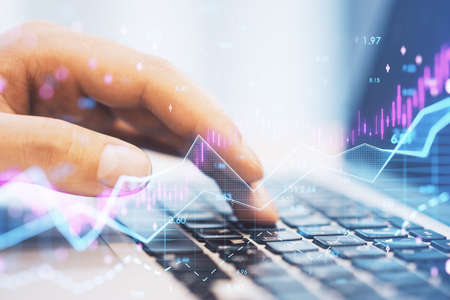 Close up of hands using laptop computer keyboard with abstract glowing candlestick forex chart with...