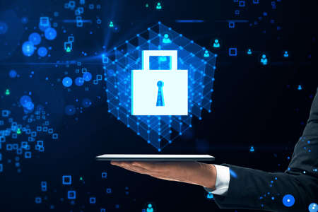 Close up of businessman hand holding tablet with creative glowing blue padlock grid hologram on...