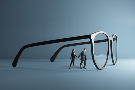 Thoughtful young businessman and woman holding hands and looking through abstract huge glasses on gray background. Clear business vision, teamwork, see through lenses in details or clean and clear business outlook concept, miniature worker looking through big eyeglass lenses to get clear visionの写真素材