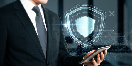 Close up of businessman hand holding cellphone with creative glowing shield hologram on blurry office interior background with various blurry icons. Cyber security, data protection concept. modern wireframe designの写真素材