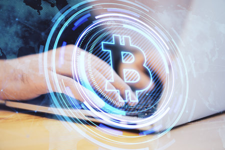 Close up of male hands at desktop using laptop with creative glowing bitcoin hologram and map on blurry background. Cryptocurrency, nft, metaverse and blockchain concept. double exposureの写真素材