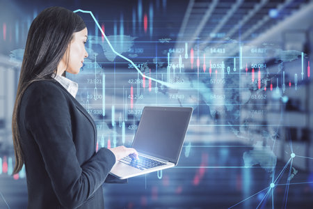 Attractive young european businesswoman using laptop with glowing candlestick forex chart and map hologram on blurry office interior background. Stock, investment, market and money concept. double exposureの写真素材