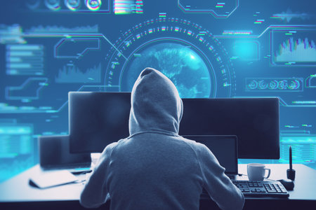 Back view of hacker in hoodie sitting at desktop with coffee cup and using computer monitors with...