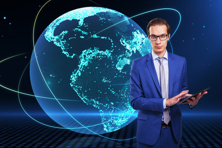 Attractive young european businessman using cellphone with creative glowing globe hologram on dark background. Technology, metaverse and digital map conceptの写真素材