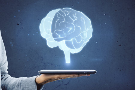 Close up of female hand holding pad with glowing human brain hologram on blurry wall background....