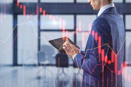 Attractive young european businessman using tablet with falling red forex hologram standing on...