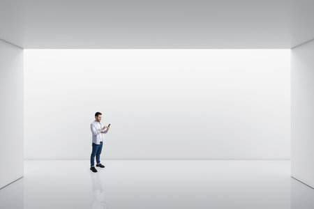 Perspective view on young man using smartphone in empty spacious area with white wall space background for your product or car presentation, mock upの写真素材