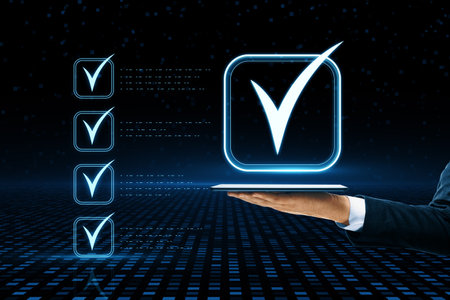 Digital check mark symbol on dark background. Checklist concept. Close up of businessman hand holding tabletの写真素材