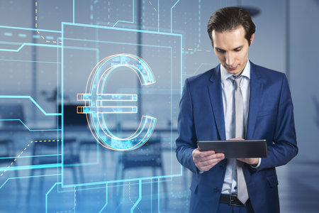 Attractive young european businessman with tablet and glowing linear euro hologram standing on blurry office interior background. Investment, trade and finance concept. double exposureの写真素材