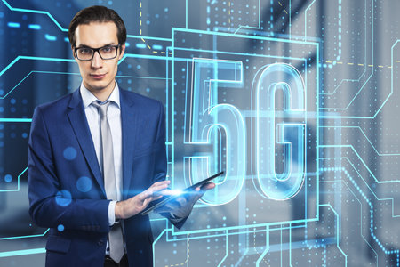 Attractive young european businessman using tablet with glowing linear 5g hologram on blurry office interior background. 5G network and wireless systems. double exposureの写真素材