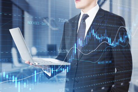 Close up of businessman hand using laptop computer with glowing candlestick forex chart with index on blurry office interior background. Trade, stock and finance concept. double exposureの写真素材