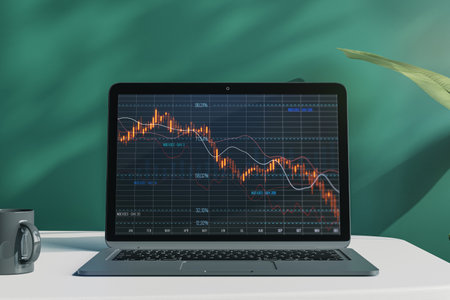 Close up of laptop computer with falling red crisis forex chart on screen. Desktop and chalkboard background. Recession, trade and downfall concept. 3D Renderingの写真素材