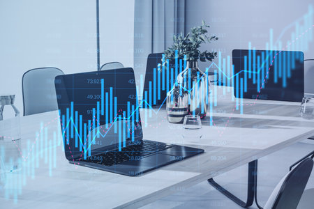 Close up of laptop on coworking desktop with glowing candlestick forex chart on blurry background....