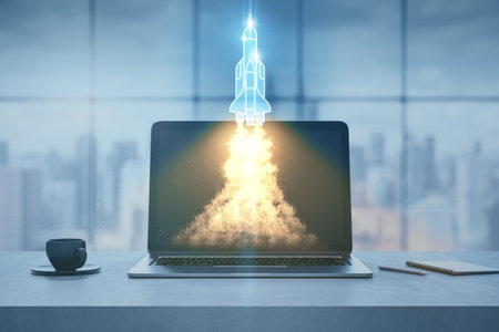 Close up of modern workplace with laptop and launching rocker hologram, coffee cup and window with blurry city view in the background. Start up, business and workspace concept. 3D Renderingの写真素材