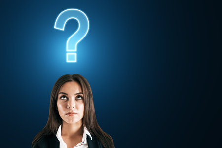 Portrait of young businesswoman looking for answers. Glowing question mark hologram above head on blue background. Stress, anxiety and confusion conceptの写真素材
