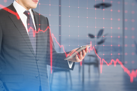 Close up of businessman hand using cellphone with falling red business graph grid on blurry office...