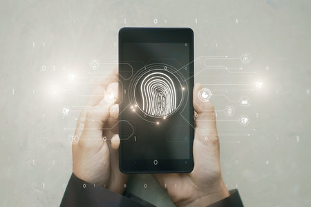 Top view of hands holding mobile phone at white desktop with glowing fingerprint hologram and icons....