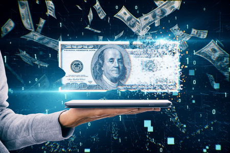Cash and traditional money disappearance, money digitalization and inflation concept with vanishing 100 dollar banknote above human hand with digital tablet on dark background under dollar rainの写真素材