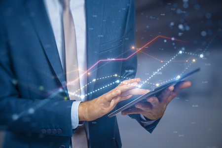 Close up of male hand using tablet with glowing business chart lines with bokeh sparkles on blurry background. Annual report, finance and success concept. double exposureの写真素材