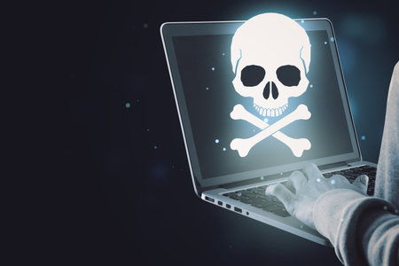 Close up of hand using laptop with glowing white skull hologram on dark background with mock up place for your text. Cyber attack and malware conceptの写真素材
