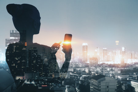 Back view of thoughtful businesswoman silhouette using cellphone while standing on dark night city background. Success, work, communication and lifestyle concept. double exposureの写真素材