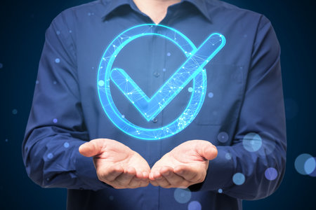 Close up of businessman hands holding glowing blue polygonal checkmark on dark blurry background. Success, business agreement, ok sign, approval conceptの写真素材