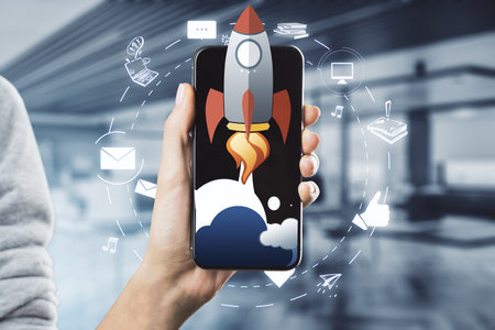 Female hand holding cellphone with creative rocket ship sketch on blurry office background. Content launch and spaceship conceptの写真素材