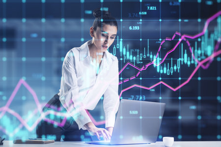 Attractive european businesswoman using laptop computer with glowing forex index chart with grid on blurry office interior background. Market, finance and online trading concept. double exposureの写真素材