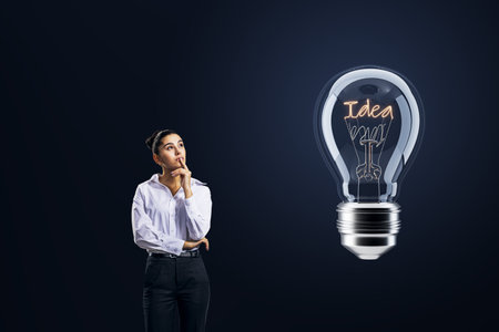 Thoughtful businesswoman looking at light bulb on dark background. idea conceptの写真素材