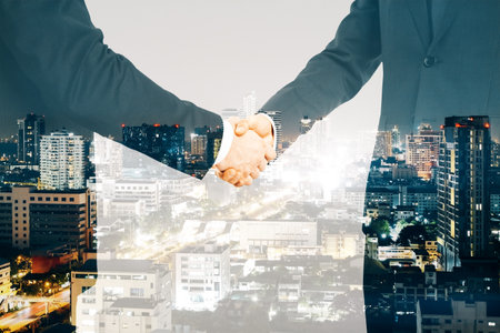 Business men shaking hands on blurry night city background. Teamwork, success and partnership concept. double exposureの写真素材