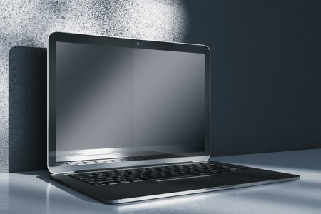 Close up of notebook computer with empty mock up screen placed on desk. Concrete wall with shadows in the background. 3D Renderingの写真素材