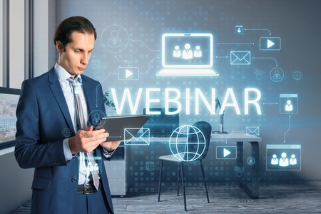 Young European businessman using tablet with creative webinar hologram on blurry office interior background. Online meeting and seminar concept. double exposureの写真素材
