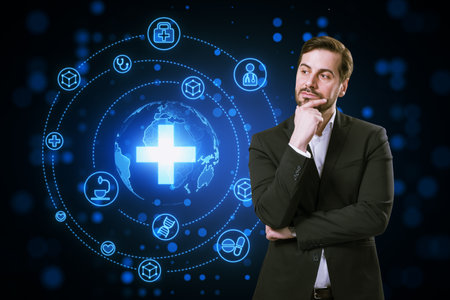 Attractive thoughtful young businessman with creative glowing blue medical hologram with cross and globe on dark background. Science, healthcare system and futuristic pharmacy conceptの写真素材