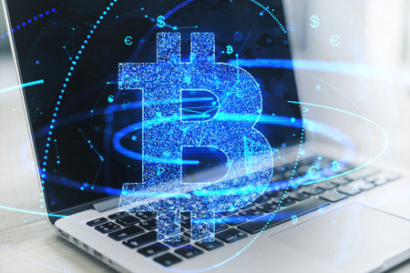 Close up of laptop with glowing bitcoin hologram on blurry background. Crypto and finance concept. Double exposureの写真素材