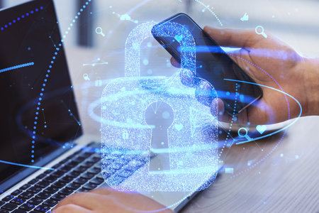 Close up of male hands using laptop and smartphone on desk with glowing padlock and globe hologram...