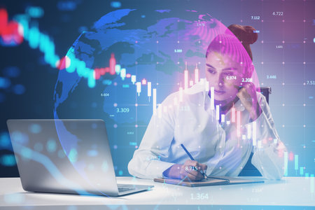 Attractive young European businesswoman sitting at desk with laptop and falling forex chart on...