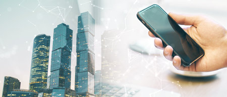 Close up of hand holding cellphone at abstract workplace with night city view on wide light...