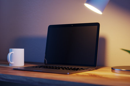 Modern blurry nighttime desktop with blank laptop screen, lamp and coffee cup. Designer workspace concept. 3D Renderingの写真素材