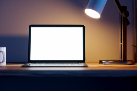 Modern blurry nighttime workplace with blank white laptop screen, lamp and coffee cup. Designer workspace concept. 3D Renderingの写真素材