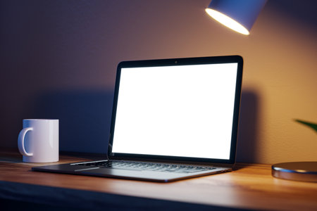 Modern blurry nighttime desktop with blank white laptop screen, lamp and coffee cup. Designer workspace concept. 3D Renderingの写真素材