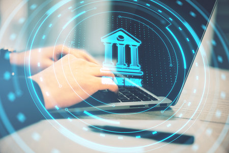 Close up of businessman using laptop on desk with pen and creative round hologram with bank on blurry background. Money, online banking and finance concept. Double exposureの写真素材