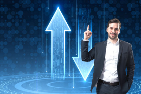 Attractive young European businessman pointing up at abstract up and down arrows on dark blue background. The concept of digital traffic or exchange. blue arrow technology backgroundの写真素材