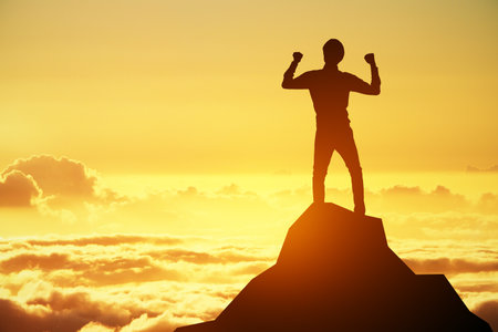 A dynamic silhouette of a person with fists up in the air on a mountain top, with sunrise depicting motivation and strengthの写真素材