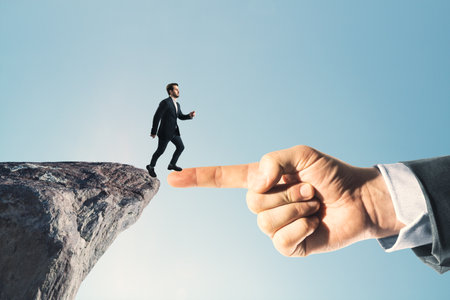 Businessman standing on cliff edge on bright blue sky background with finger bridge. Future, success and tomorrow conceptの写真素材
