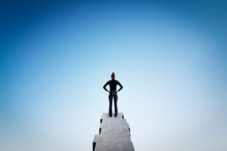 Back view of young woman standing on edge and looking at bright blue city sky with mock up place. Future, success, think and tomorrow conceptの写真素材